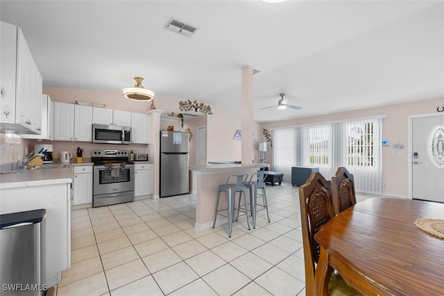 kitchen with appliances with stainless steel finishes, a kitchen bar, sink, ceiling fan, and white cabinets