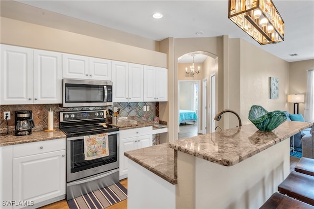 kitchen with appliances with stainless steel finishes, a kitchen island, hanging light fixtures, and white cabinetry