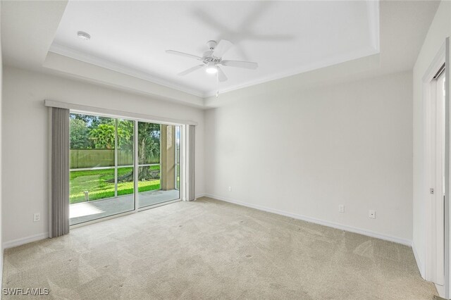 spare room featuring a tray ceiling, light colored carpet, ornamental molding, and ceiling fan