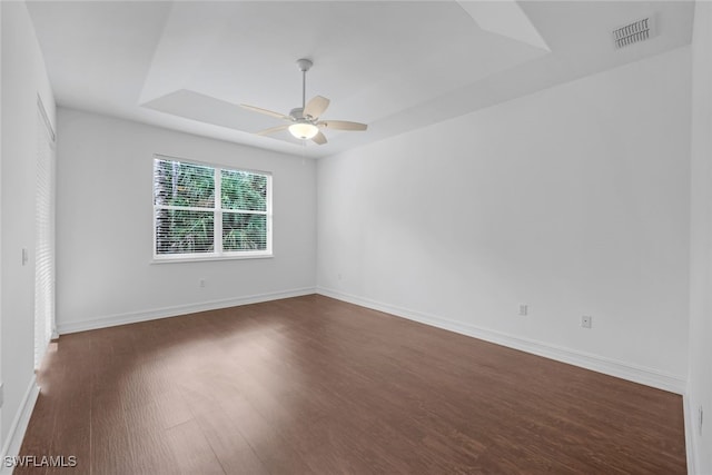 spare room with a tray ceiling, ceiling fan, and dark hardwood / wood-style floors