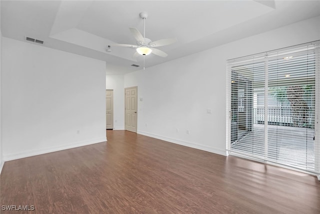 empty room with dark hardwood / wood-style flooring, a raised ceiling, and ceiling fan