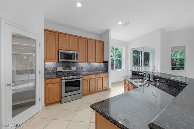 kitchen with backsplash, dark stone counters, sink, appliances with stainless steel finishes, and light tile patterned flooring