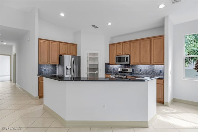 kitchen with decorative backsplash, appliances with stainless steel finishes, dark stone countertops, and an island with sink