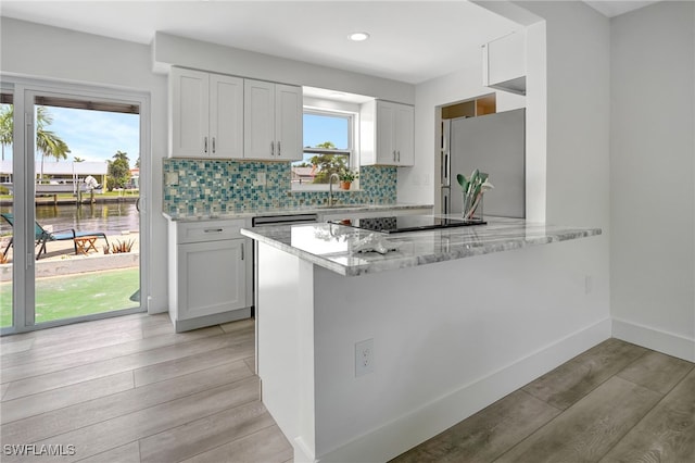 kitchen with white cabinets, stainless steel fridge, light wood-type flooring, and kitchen peninsula