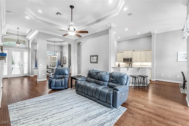 living room featuring a raised ceiling, ceiling fan with notable chandelier, wood-type flooring, crown molding, and sink