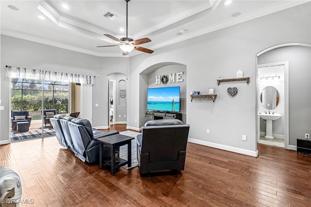 living room featuring dark hardwood / wood-style floors, a tray ceiling, ornamental molding, sink, and ceiling fan