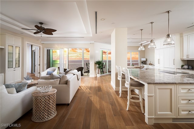 living room featuring ceiling fan, ornamental molding, dark hardwood / wood-style flooring, and a tray ceiling