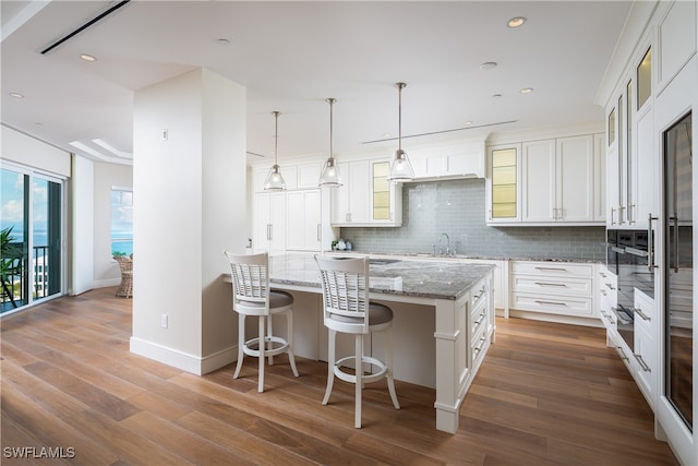 kitchen featuring white cabinetry, decorative light fixtures, decorative backsplash, hardwood / wood-style floors, and a center island