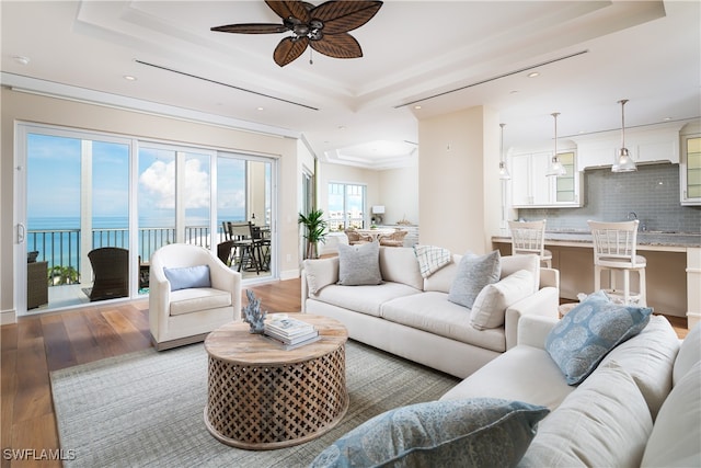 living room featuring light wood-type flooring, a water view, and a raised ceiling