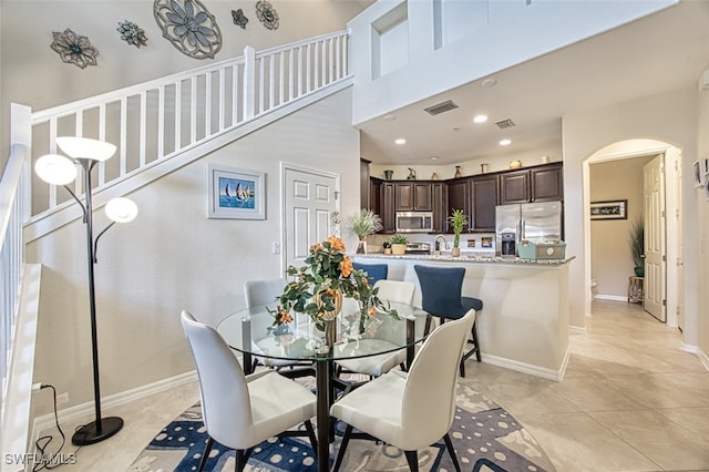 dining space with arched walkways, light tile patterned flooring, a towering ceiling, visible vents, and baseboards