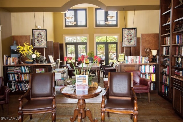 living area with arched walkways, french doors, bookshelves, and wood finished floors