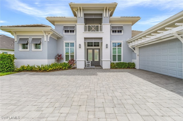 view of front of house with french doors, decorative driveway, a balcony, and stucco siding