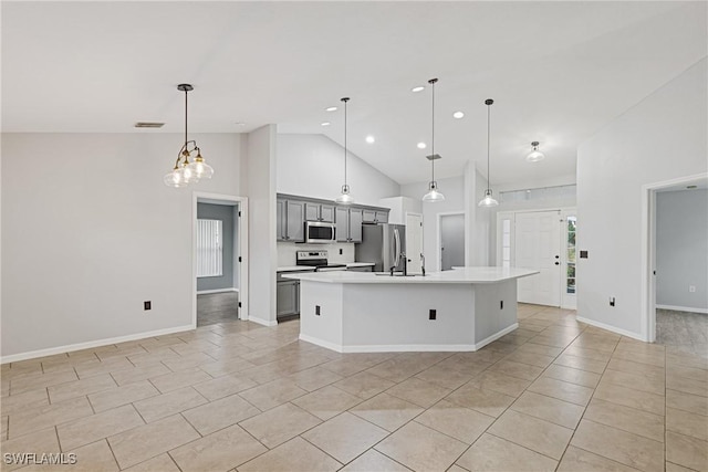 kitchen with gray cabinetry, stainless steel appliances, light tile patterned floors, hanging light fixtures, and an island with sink