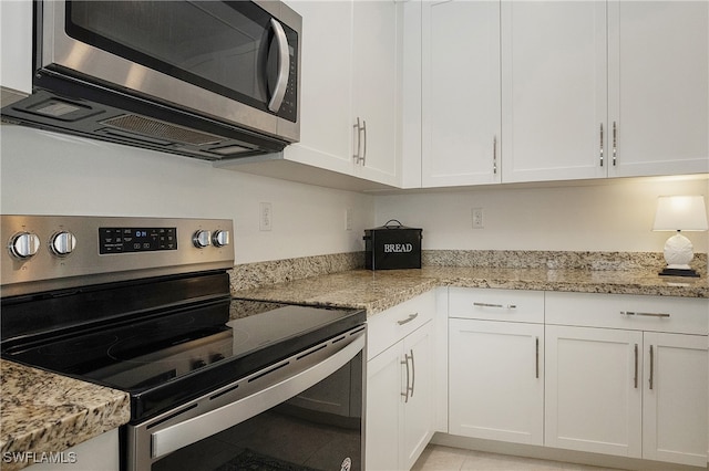 kitchen with light tile patterned floors, appliances with stainless steel finishes, light stone counters, and white cabinetry