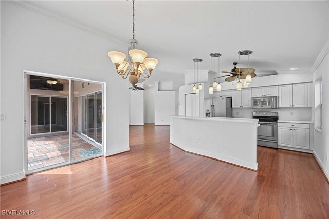 kitchen with stainless steel appliances, ceiling fan with notable chandelier, hardwood / wood-style flooring, and decorative light fixtures