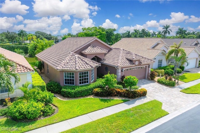 mediterranean / spanish house featuring a tiled roof, a front yard, stucco siding, decorative driveway, and an attached garage