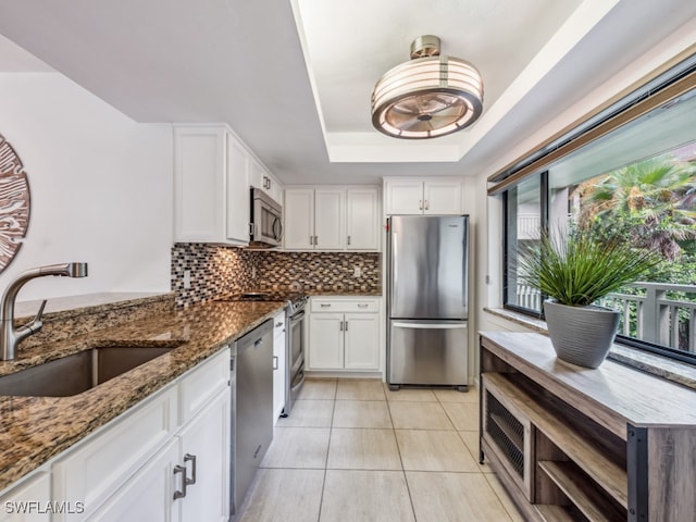 kitchen featuring stainless steel appliances, a raised ceiling, sink, dark stone countertops, and white cabinets