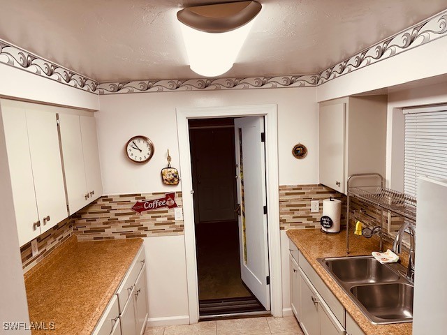 kitchen with white cabinetry, backsplash, light tile patterned flooring, and sink