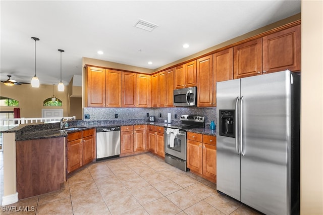 kitchen with appliances with stainless steel finishes, dark stone countertops, backsplash, kitchen peninsula, and pendant lighting