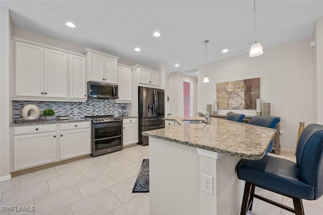 kitchen with a center island with sink, appliances with stainless steel finishes, hanging light fixtures, sink, and white cabinetry