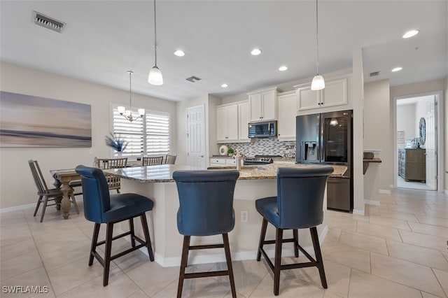 kitchen featuring white cabinets, a notable chandelier, black fridge, pendant lighting, and a center island with sink