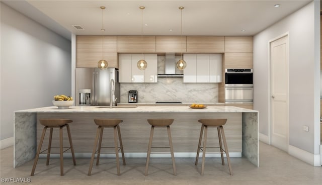 kitchen with a kitchen breakfast bar, appliances with stainless steel finishes, a kitchen island with sink, and wall chimney range hood