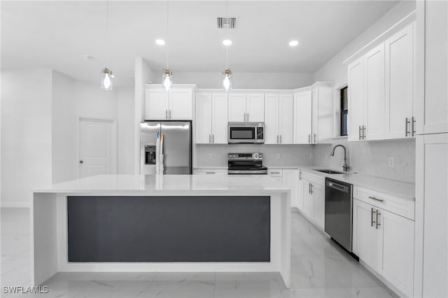 kitchen with decorative light fixtures, appliances with stainless steel finishes, a center island, sink, and white cabinetry