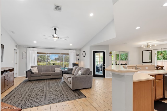 living room featuring lofted ceiling, ceiling fan with notable chandelier, sink, and light hardwood / wood-style flooring