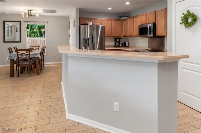 kitchen featuring stainless steel appliances, an inviting chandelier, light wood-type flooring, and decorative backsplash