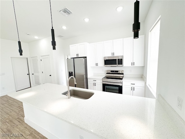 kitchen with light wood-type flooring, appliances with stainless steel finishes, white cabinetry, and pendant lighting