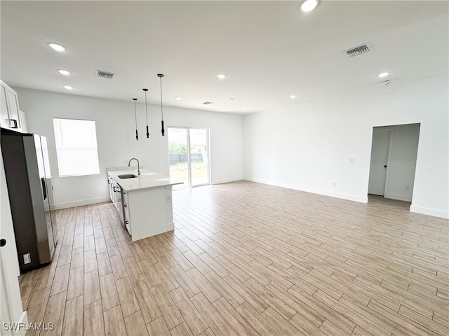 kitchen featuring light hardwood / wood-style flooring, decorative light fixtures, white cabinetry, a center island with sink, and stainless steel fridge with ice dispenser