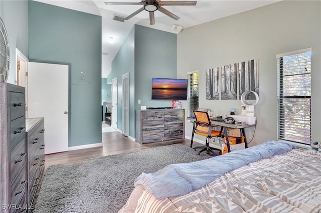 bedroom with multiple windows, ceiling fan, hardwood / wood-style floors, and a towering ceiling