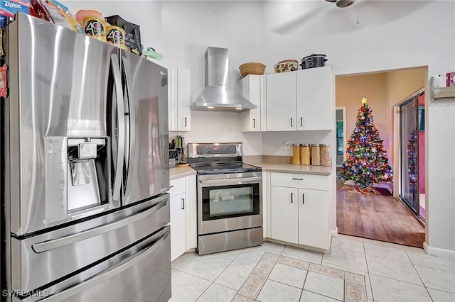 kitchen featuring wall chimney exhaust hood, ceiling fan, light wood-type flooring, appliances with stainless steel finishes, and white cabinetry