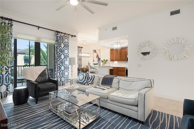 living room with ceiling fan with notable chandelier, crown molding, and light tile patterned floors