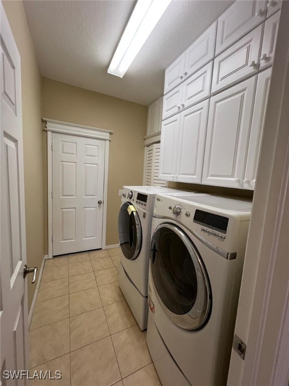 laundry room featuring cabinets, light tile patterned floors, separate washer and dryer, and a textured ceiling