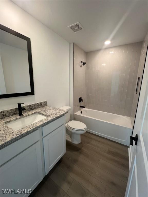 full bathroom with wood-type flooring, toilet, tiled shower / bath combo, and vanity