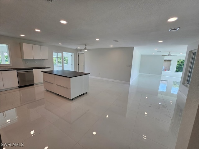 kitchen with light tile patterned floors, a center island, ceiling fan, stainless steel dishwasher, and white cabinets