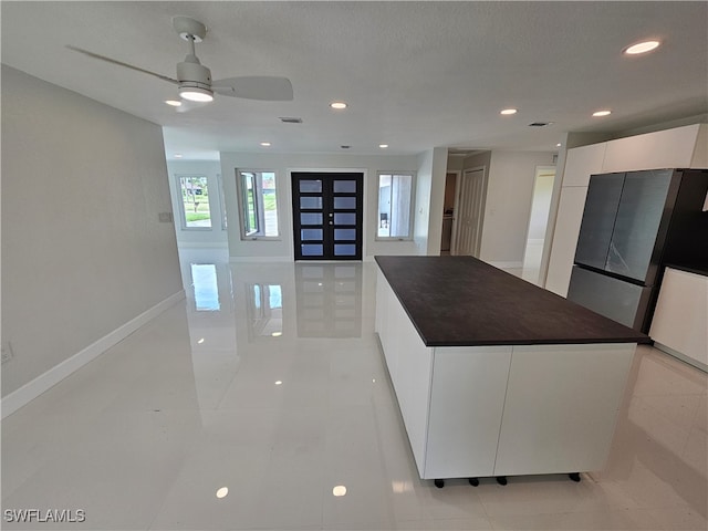 kitchen with a textured ceiling, a center island, white cabinetry, ceiling fan, and light tile patterned flooring