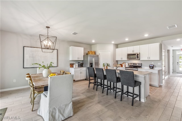 kitchen with white cabinets, stainless steel appliances, a center island with sink, and light hardwood / wood-style floors