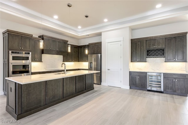 kitchen with beverage cooler, sink, hanging light fixtures, appliances with stainless steel finishes, and light hardwood / wood-style floors