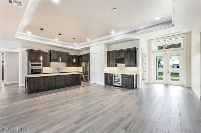 kitchen with beverage cooler, a tray ceiling, appliances with stainless steel finishes, and light hardwood / wood-style flooring