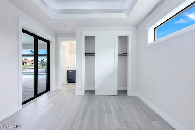 unfurnished bedroom with a tray ceiling, french doors, a closet, and light hardwood / wood-style floors