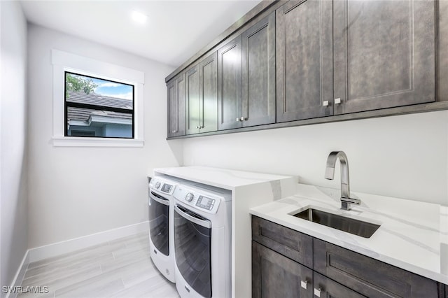 laundry room featuring washing machine and clothes dryer, cabinets, sink, and light hardwood / wood-style flooring