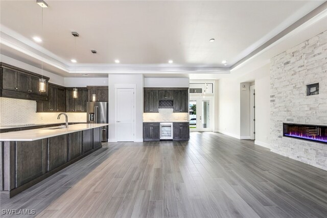 kitchen featuring hardwood / wood-style floors, wine cooler, hanging light fixtures, a tray ceiling, and dark brown cabinetry