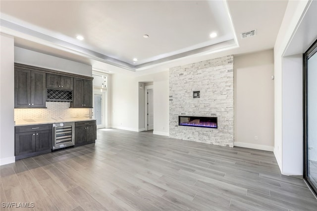 unfurnished living room with a fireplace, beverage cooler, a tray ceiling, and light hardwood / wood-style floors