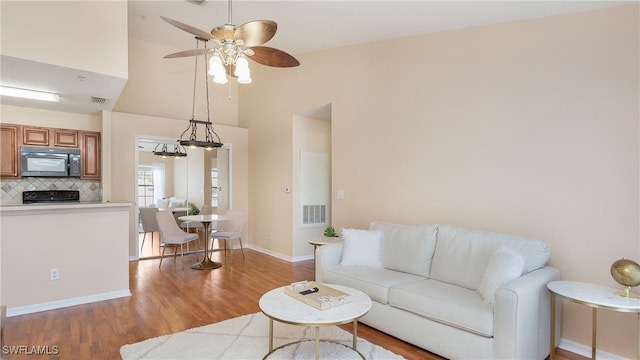 living room featuring ceiling fan with notable chandelier, light wood-type flooring, and high vaulted ceiling