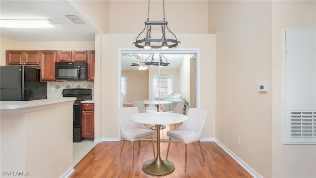 kitchen featuring light wood-type flooring, black appliances, decorative light fixtures, and backsplash