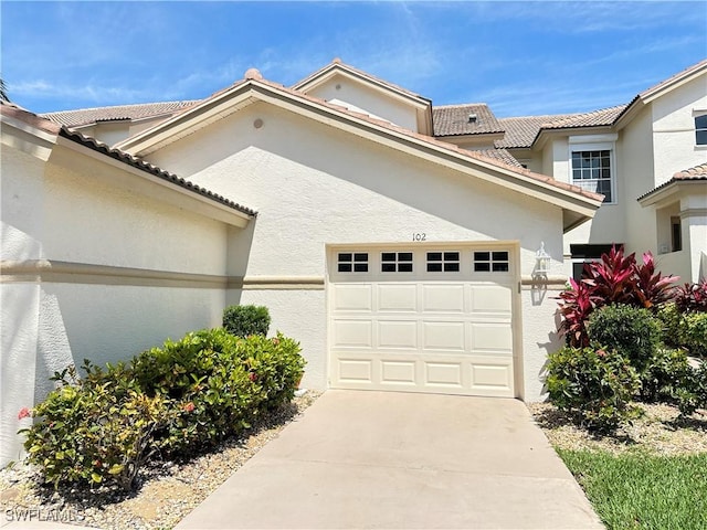 view of front of property with a garage, a tile roof, concrete driveway, and stucco siding