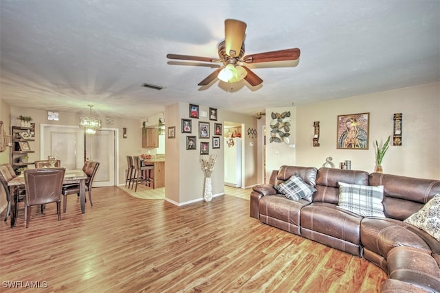 living room featuring ceiling fan with notable chandelier and light hardwood / wood-style floors