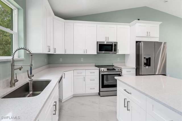 kitchen with appliances with stainless steel finishes, white cabinetry, light stone countertops, lofted ceiling, and sink